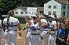 Softball players in white uniforms stand on a field as one holds a 'State Bound' sign.