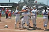 Softball players in blue and white uniforms celebrate near home plate on a dirt field.