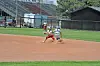 Two players run across a dirt baseball infield near a dugout and bleachers.