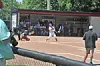 Youth baseball players on a dirt field with spectators watching from behind a fence.