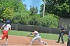 Youth baseball player in red slides toward a base while a fielder in white and blue attempts a tag.
