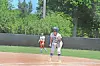 Softball player standing on the base path with a fielder in the background on a sunny field.
