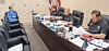Officials seated behind a curved table with microphones and papers in a meeting room.