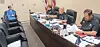 Officials seated behind a curved table with microphones and papers in a meeting room.