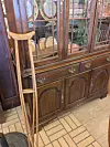 Wooden cabinet with glass doors, dishes inside, and crutches leaning against it on a tiled floor.