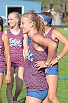 Cheerleaders in blue and red uniforms stand together on a grassy field outdoors.