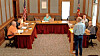 People seated around tables in a council chamber while one man stands speaking.