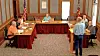 People seated around tables in a council chamber while one man stands speaking.