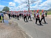 A marching band marches along a road beside a puddle under a partly cloudy sky.