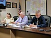 Three officials seated at a conference table reading and writing on documents in an office.