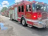 Red fire trucks parked along a street, with the front truck closest to the camera and a firefighter visible inside.