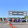 People gather beneath a START / FINISH banner beside orange cones and a parked van on a road.