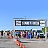 People gather beneath a START / FINISH banner beside orange cones and a parked van on a road.