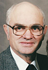 Close-up portrait of an older man wearing glasses and formal clothing.