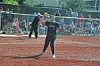 Softball batter in the foreground at home plate with spectators behind a fence.