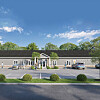 Screenshot of a low commercial building with parked cars in front and trees under a blue sky.