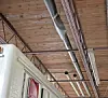 Partial view of a white vehicle under a wooden ceiling with exposed pipes and ductwork.