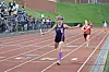 Runner in purple crosses the finish line on an outdoor track with other runners behind.