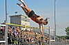 An athlete in red and black is airborne over a high jump bar at a track meet.