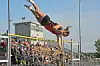 An athlete in red and black is airborne over a high jump bar at a track meet.