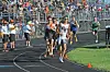 Several runners compete on a track as a crowd watches from the stands.