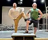Two performers pose on a stage, each with one foot raised on a platform under bright stage lights.