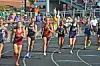 Runners race down a street past spectators and barriers in an outdoor event.