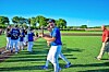 People in blue baseball uniforms gathered on a sunny grass field.