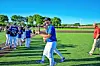 People in blue baseball uniforms gathered on a sunny grass field.