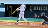 Baseball batter swinging as catcher crouches behind home plate in a stadium.