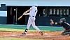 Baseball batter swinging as catcher crouches behind home plate in a stadium.