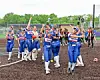Softball players in blue uniforms celebrate together on a field with raised arms.