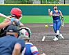 Softball pitcher in blue throws toward home plate with players in the foreground.