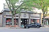 Black sedan parked outside a storefront with large windows and trees lining the sidewalk.
