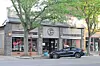 Black sedan parked outside a storefront with large windows and trees lining the sidewalk.
