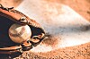 Close-up of a baseball glove next to a baseball on dirt.