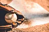 Close-up of a baseball glove next to a baseball on dirt.