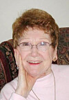 Smiling elderly woman with glasses resting her hand on her cheek.