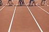Sprinters crouch in starting blocks on a red running track before a race.