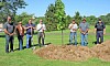 A group of people standing beside a mound of dirt and a freshly dug grave in a cemetery.