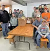 A group of people gathered around cardboard boxes on a cafeteria table in a cafeteria.