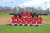 A youth baseball team poses in red uniforms on a baseball field with coaches standing behind them.