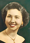 Studio portrait of a smiling woman wearing gold jewelry against a dark background.