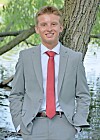 Young man in a gray suit and red tie standing outdoors beside a tree.