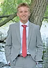 Young man in a gray suit and red tie standing outdoors beside a tree.