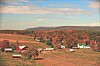 Rural fields with scattered barns and houses in an autumn landscape beneath hills and clouds.