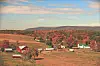 Rural fields with scattered barns and houses in an autumn landscape beneath hills and clouds.