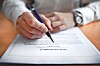 Close-up of a hand holding a pen over a printed document on a table.