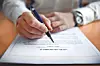 Close-up of a hand holding a pen over a printed document on a table.