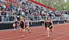 Track athletes sprint on a stadium track with a crowd watching from the bleachers.